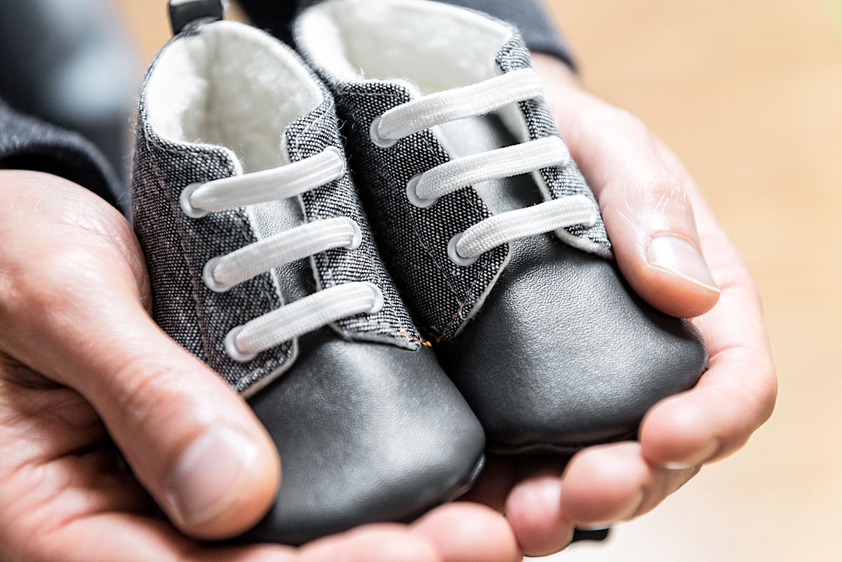 Väterliche Hände halten schwarze Lederschuhe für ein Baby in der Hand